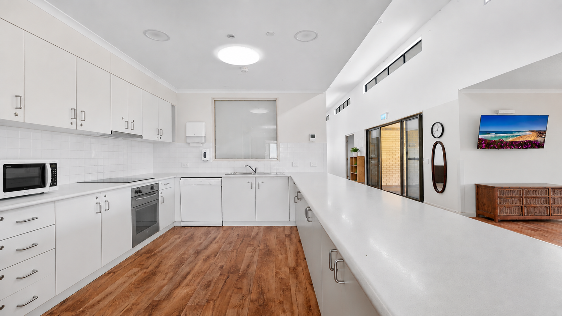 U-shaped kitchen with hard wood flooring, white bench tops, plenty of cupboard spaces, oven, stove top, and other modern appliances.